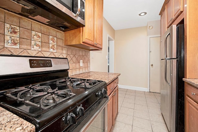 kitchen with light tile patterned flooring, light stone countertops, appliances with stainless steel finishes, baseboards, and tasteful backsplash
