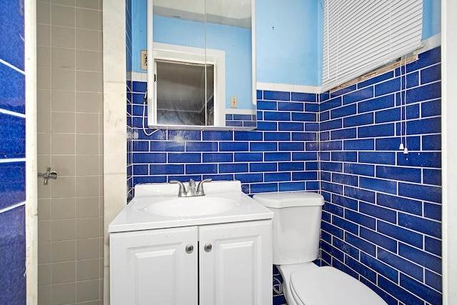 half bathroom featuring toilet, tile walls, and vanity
