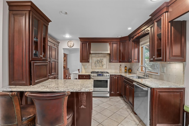 kitchen featuring decorative backsplash, a peninsula, wall chimney exhaust hood, a sink, and stainless steel appliances