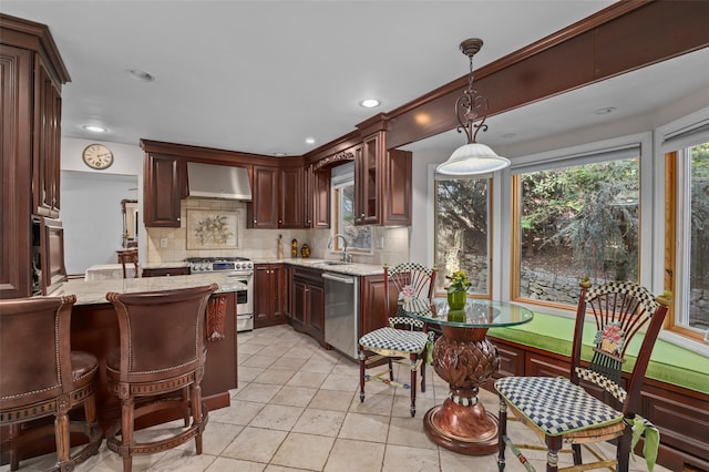 kitchen featuring pendant lighting, light stone countertops, wall chimney exhaust hood, appliances with stainless steel finishes, and backsplash