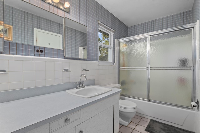 full bathroom with vanity, toilet, tile walls, bath / shower combo with glass door, and tile patterned floors