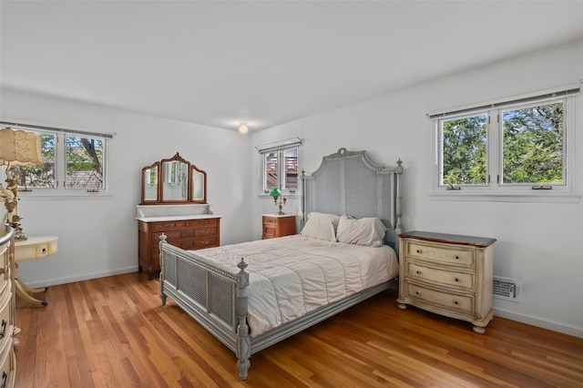 bedroom with baseboards, light wood finished floors, and visible vents