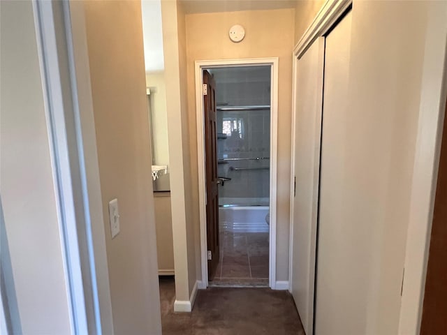 corridor with baseboards and dark colored carpet