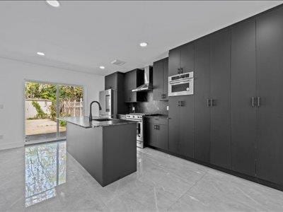 66-39 Jay Ave, Maspeth, NY 11378 - kitchen with wall chimney range hood, a center island with sink, stainless steel range, marble finish floor, and dark cabinets