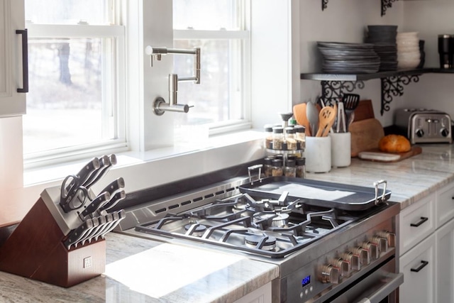 kitchen with light stone counters, stainless steel gas stove, white cabinets, and a toaster