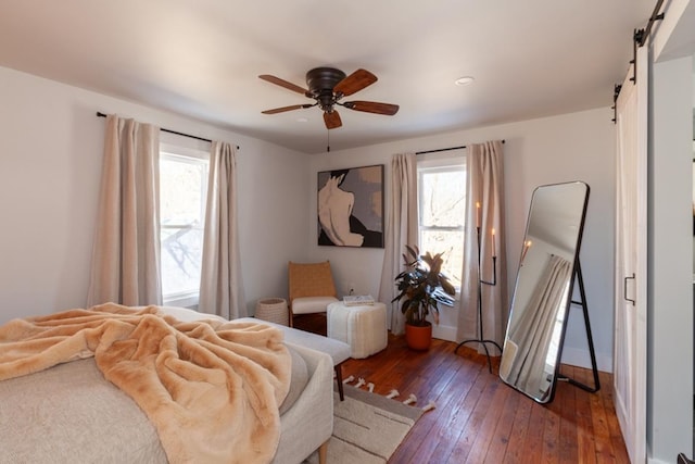 bedroom featuring hardwood / wood-style flooring, a barn door, ceiling fan, and multiple windows