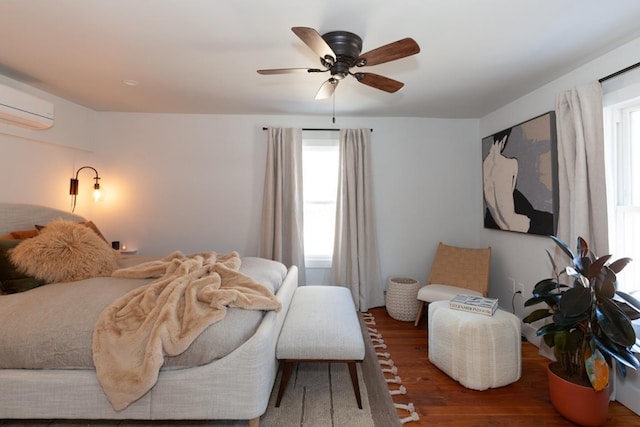 bedroom featuring a wall mounted air conditioner, a ceiling fan, wood finished floors, and multiple windows
