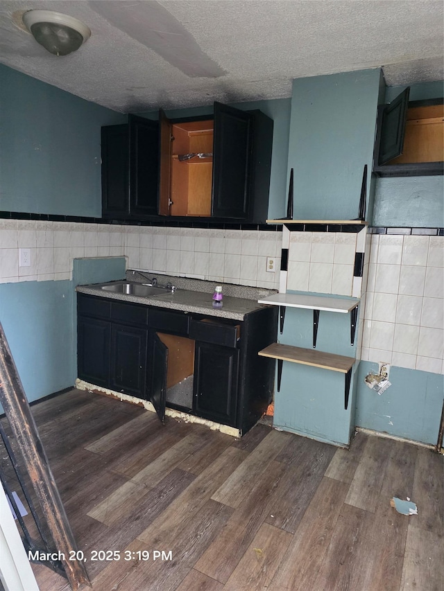 kitchen with tile walls, open shelves, wood finished floors, a sink, and dark cabinetry