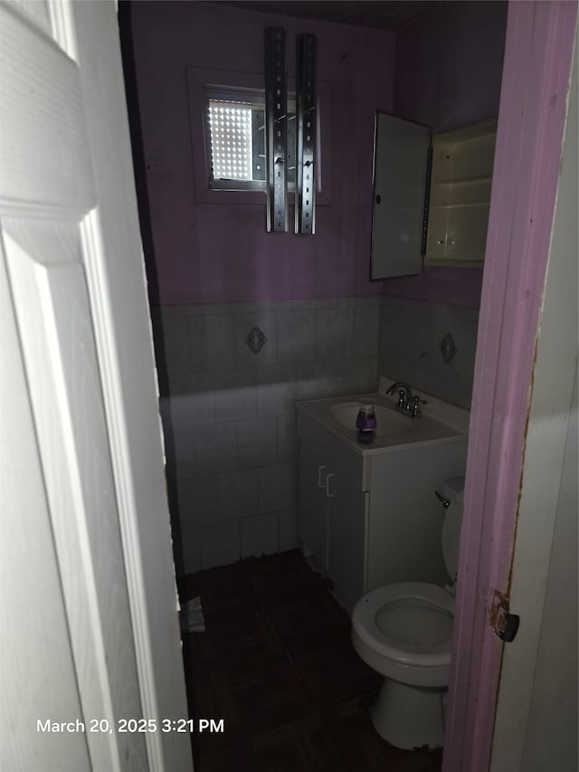 bathroom featuring vanity, wainscoting, toilet, and tile walls