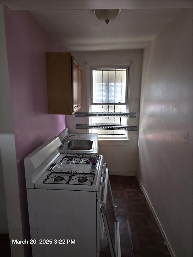 kitchen featuring baseboards, white gas stove, and a sink