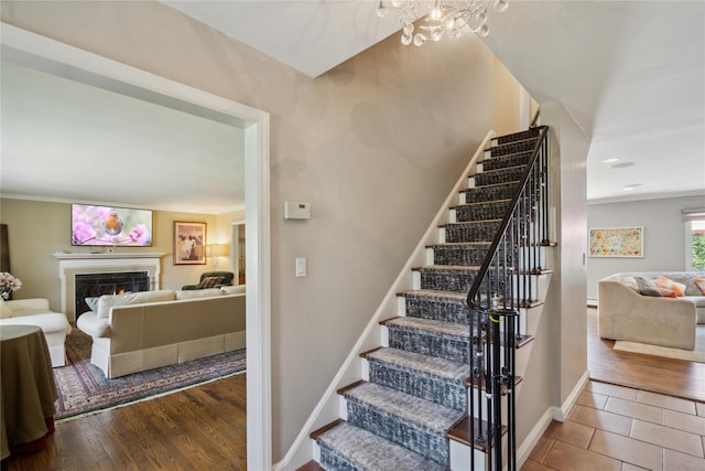 26 Woodgreen Ln, East Hills, NY 11577 - staircase featuring a chandelier, a warm lit fireplace, baseboards, and wood finished floors