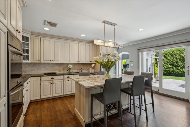 26 Woodgreen Ln, East Hills, NY 11577 - kitchen with cream cabinets, arched walkways, dark wood finished floors, a kitchen breakfast bar, and decorative backsplash