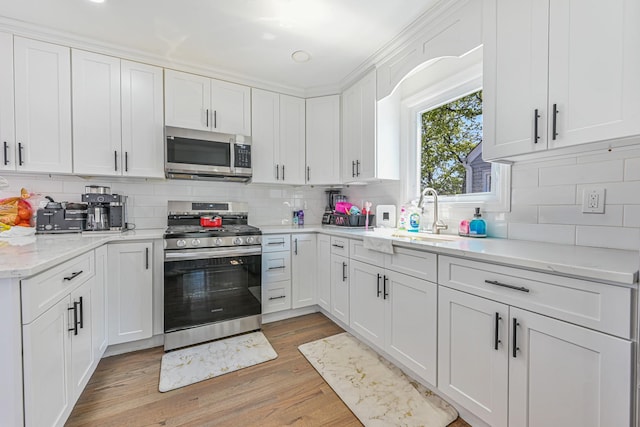 kitchen featuring white cabinets, tasteful backsplash, a sink, light wood finished floors, and appliances with stainless steel finishes