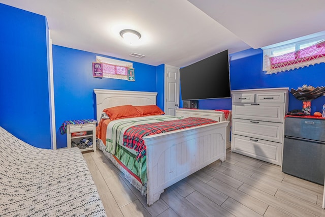 bedroom featuring visible vents, freestanding refrigerator, and wood finish floors
