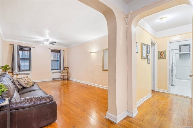 living area featuring baseboards, a ceiling fan, arched walkways, and light wood-style flooring
