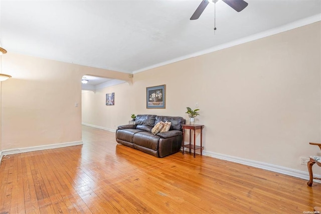 living area featuring light wood-style floors, baseboards, ceiling fan, and crown molding