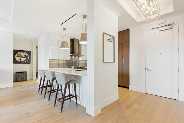 kitchen featuring wall chimney range hood, decorative backsplash, a kitchen bar, modern cabinets, and light countertops