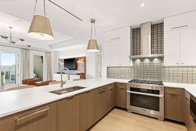 kitchen with a sink, light countertops, wall chimney exhaust hood, high end stove, and light wood-type flooring