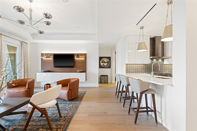 living area featuring baseboards, a tray ceiling, light wood-type flooring, and a chandelier