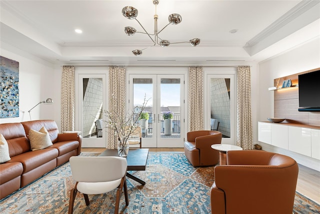 living room featuring ornamental molding, wood finished floors, a chandelier, a tray ceiling, and french doors