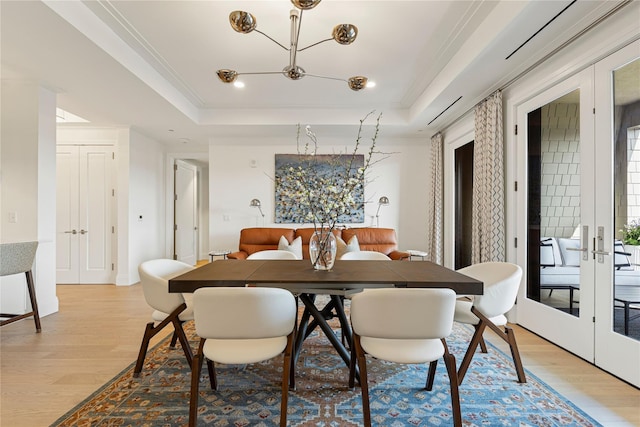 dining room featuring french doors, light wood-style flooring, a raised ceiling, and a chandelier