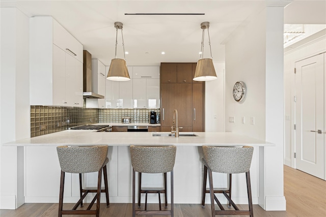 kitchen featuring a sink, modern cabinets, a peninsula, and wall chimney exhaust hood
