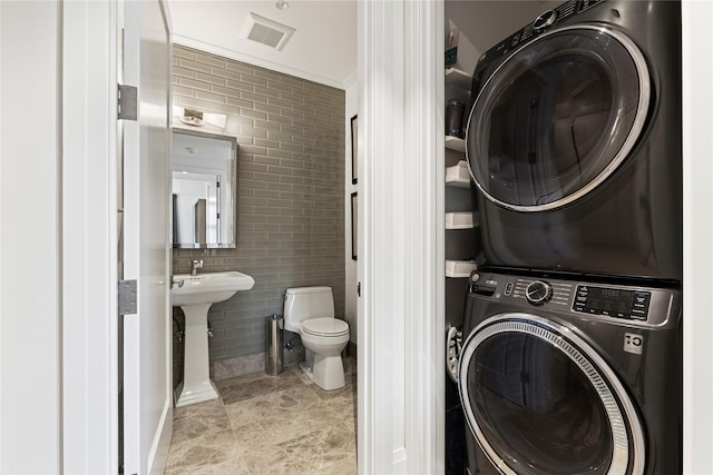 bathroom with toilet, tile walls, stacked washer and clothes dryer, and visible vents