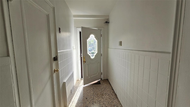 doorway with tile walls, speckled floor, and a wainscoted wall