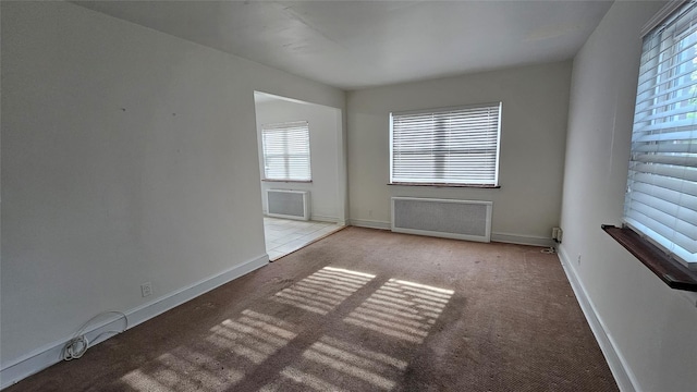 unfurnished room with carpet flooring, a wealth of natural light, and radiator heating unit
