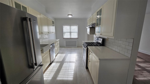 kitchen featuring light countertops, stainless steel appliances, backsplash, under cabinet range hood, and glass insert cabinets