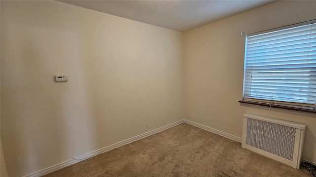 spare room featuring carpet flooring, baseboards, and radiator