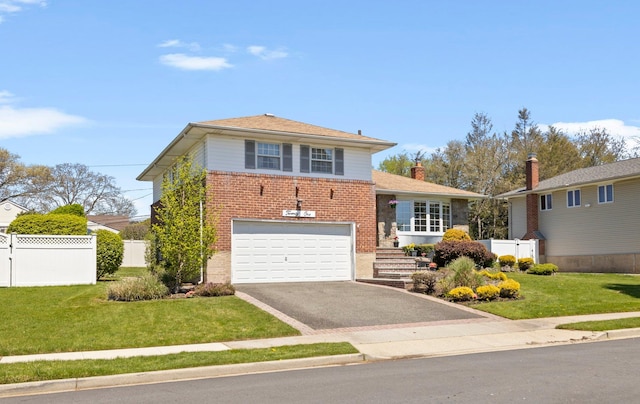 split level home with fence, an attached garage, a front lawn, brick siding, and driveway