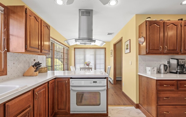 kitchen featuring island range hood, light countertops, a peninsula, marble finish floor, and oven