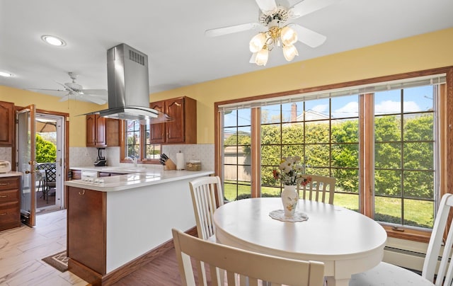 kitchen with decorative backsplash, a ceiling fan, island range hood, light countertops, and a peninsula