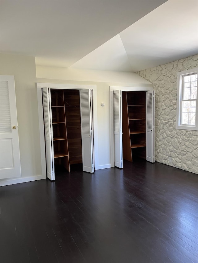 unfurnished bedroom featuring multiple closets, baseboards, and dark wood-style floors