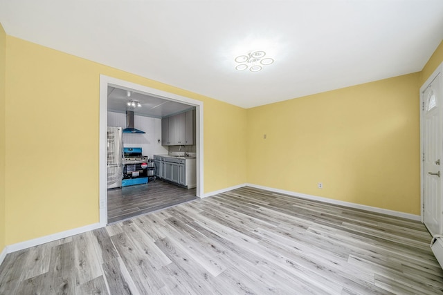 unfurnished living room with baseboards, a sink, light wood-style flooring, and a baseboard radiator