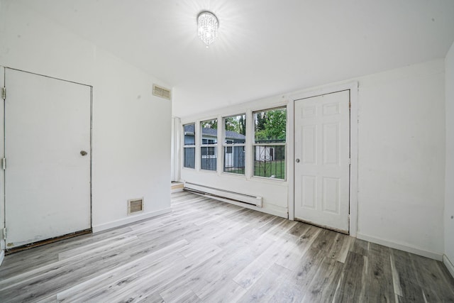 interior space with a baseboard heating unit, wood finished floors, and visible vents
