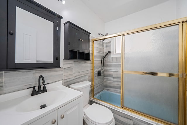 bathroom featuring vanity, combined bath / shower with glass door, toilet, and tile walls