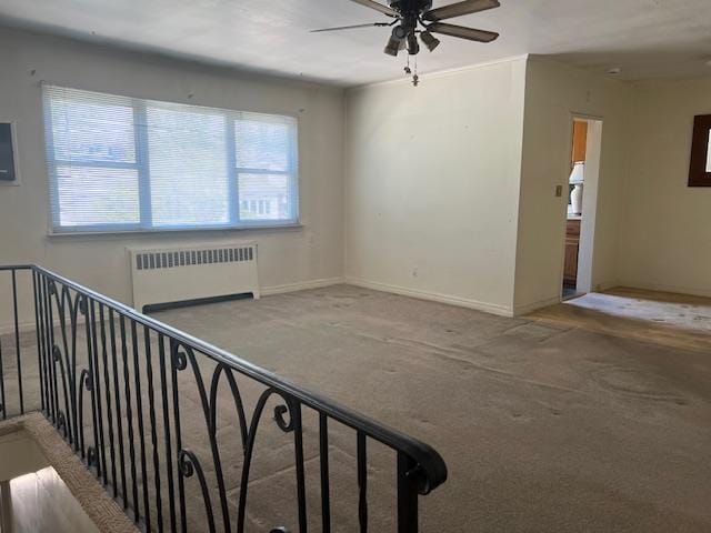 empty room with carpet floors, radiator, ceiling fan, and baseboards