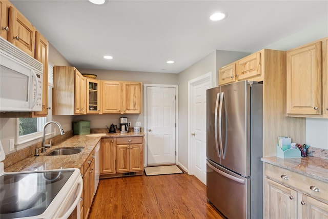 kitchen with a sink, light brown cabinetry, white appliances, and wood finished floors