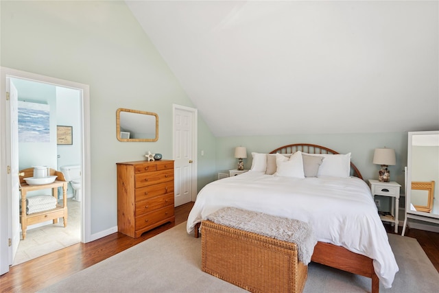 bedroom featuring ensuite bath, wood finished floors, and vaulted ceiling