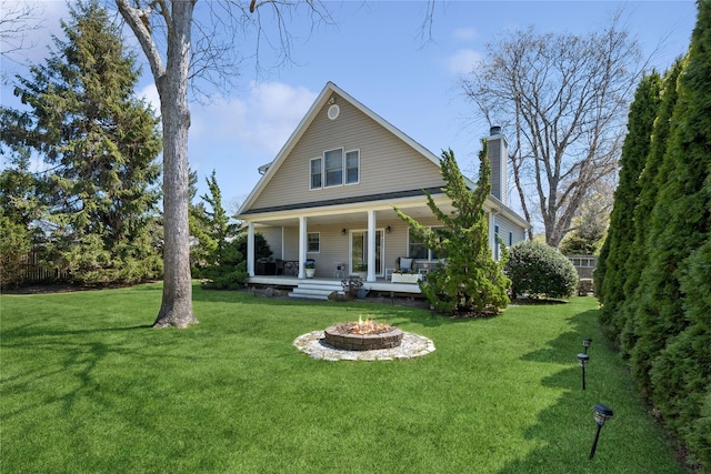 back of house featuring covered porch, a lawn, a chimney, and an outdoor fire pit
