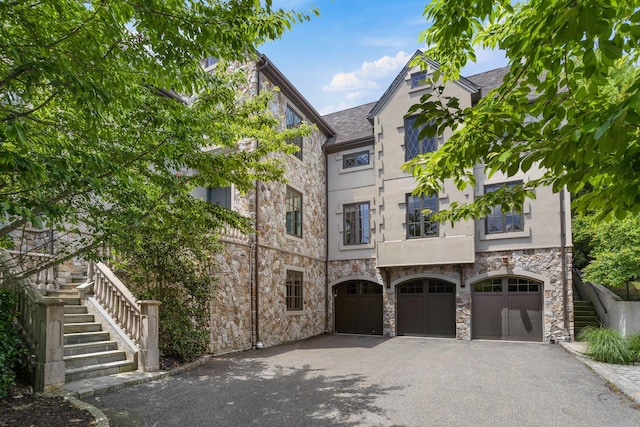 view of front of house with a garage, stairway, aphalt driveway, and stone siding