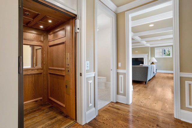 corridor featuring elevator, wood finished floors, beamed ceiling, ornamental molding, and coffered ceiling