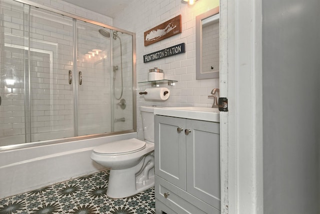 bathroom with tile walls, enclosed tub / shower combo, vanity, and toilet