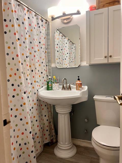 full bath featuring toilet, wood finished floors, and a shower with shower curtain