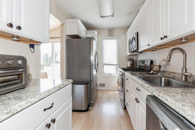 kitchen with white cabinets, a sink, stainless steel appliances, light wood-type flooring, and a toaster