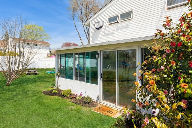 view of home's exterior with a sunroom, a lawn, and fence