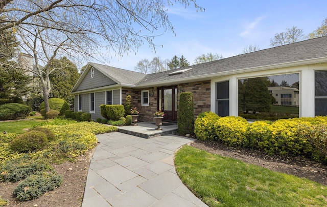 ranch-style home featuring a shingled roof and stone siding