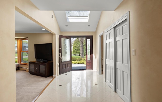 foyer entrance featuring visible vents, tile patterned flooring, a baseboard heating unit, and vaulted ceiling with skylight